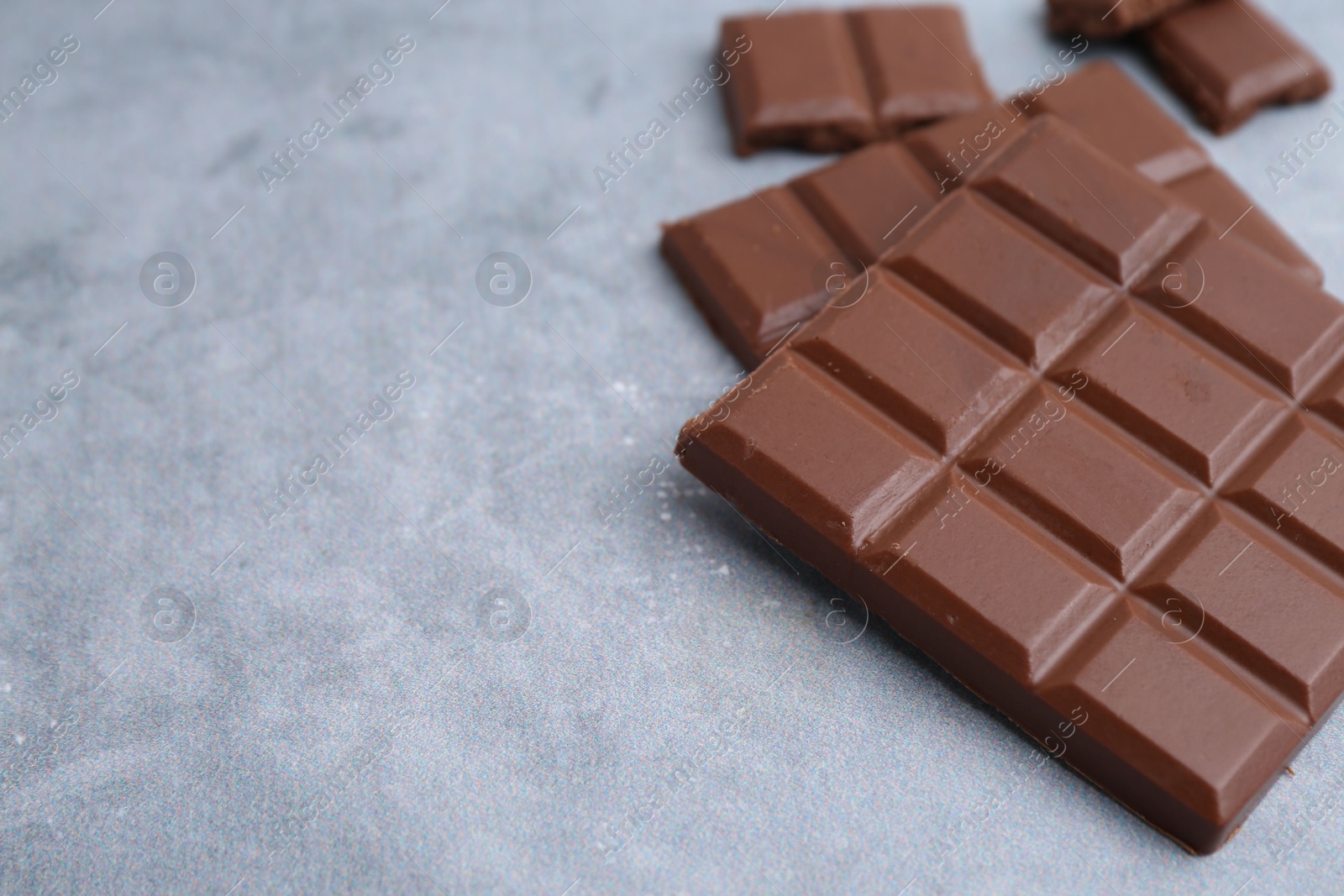 Photo of Pieces of delicious milk chocolate on grey table, closeup. Space for text