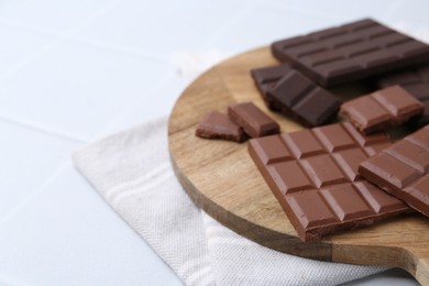 Photo of Different types of chocolate on white tiled table, closeup. Space for text