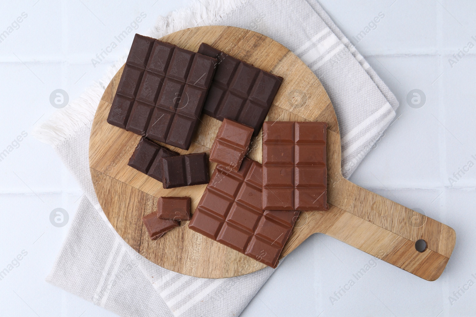 Photo of Different types of chocolate on white tiled table, top view