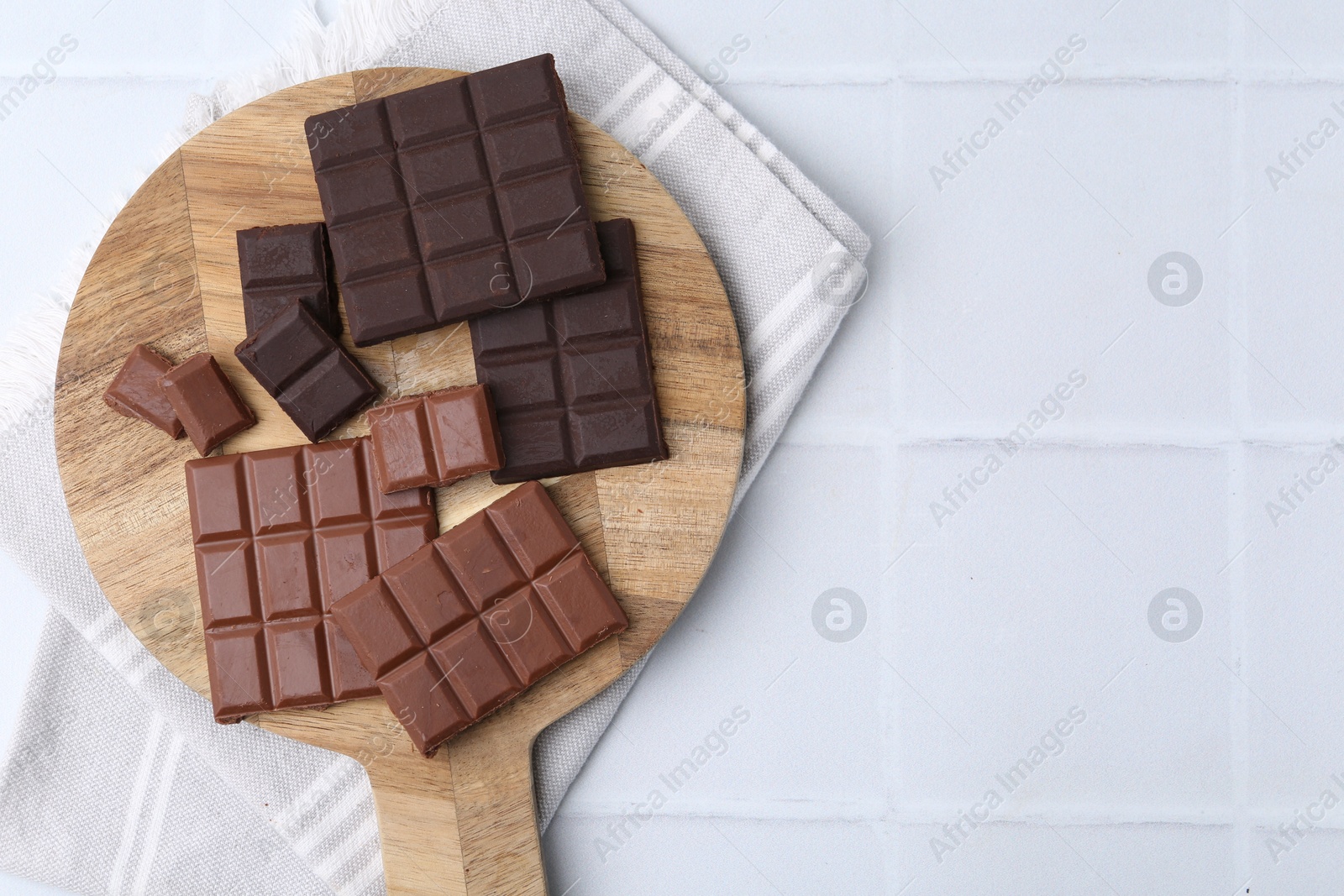 Photo of Different types of chocolate on white tiled table, top view. Space for text