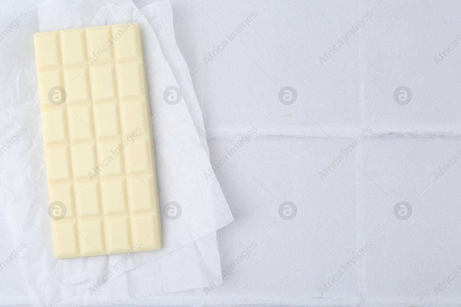 Photo of Delicious white chocolate bar on tiled table, top view. Space for text