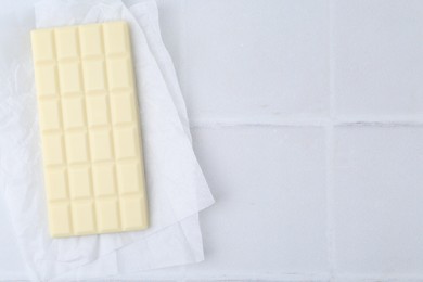 Photo of Delicious white chocolate bar on tiled table, top view. Space for text