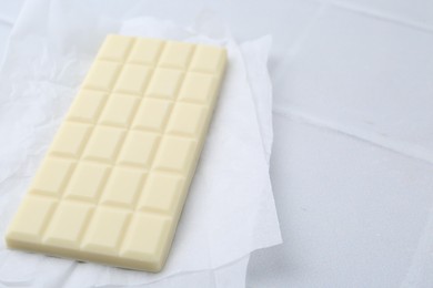 Photo of Delicious white chocolate bar on tiled table. Space for text