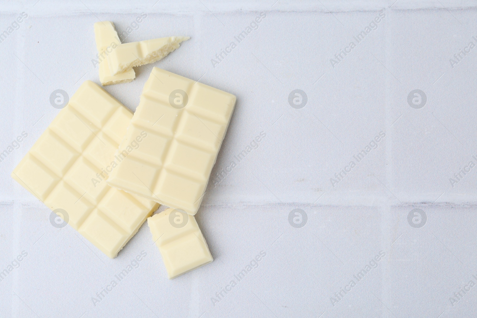 Photo of Pieces of delicious white chocolate on tiled table, top view. Space for text