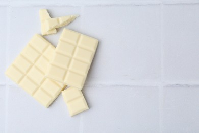 Photo of Pieces of delicious white chocolate on tiled table, top view. Space for text