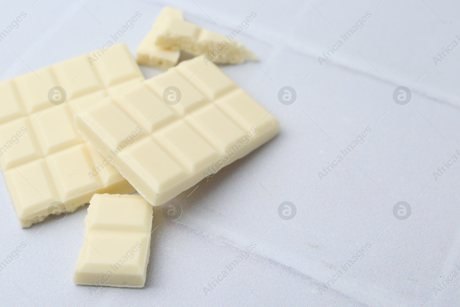 Photo of Pieces of delicious white chocolate on tiled table, closeup. Space for text