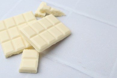 Photo of Pieces of delicious white chocolate on tiled table, closeup. Space for text