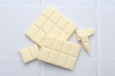 Photo of Pieces of delicious white chocolate on tiled table, top view