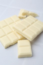 Photo of Pieces of delicious white chocolate on tiled table, closeup