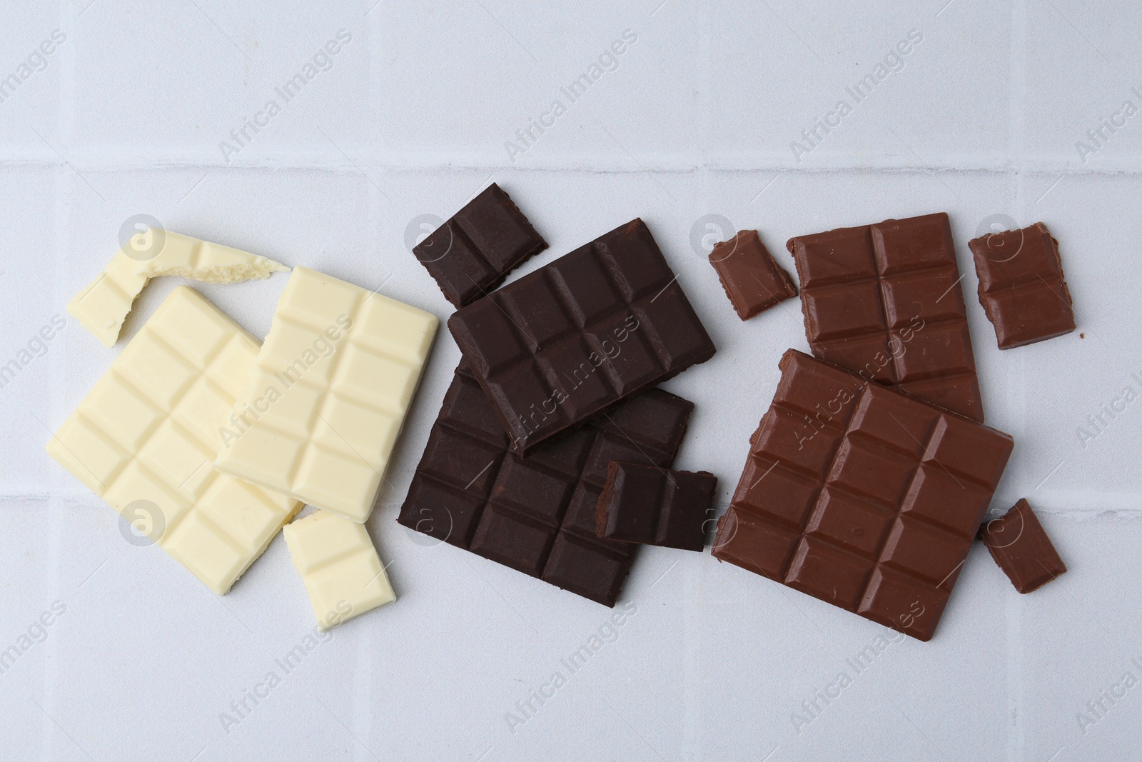 Photo of Different types of chocolate on white tiled table, flat lay