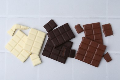 Photo of Different types of chocolate on white tiled table, flat lay