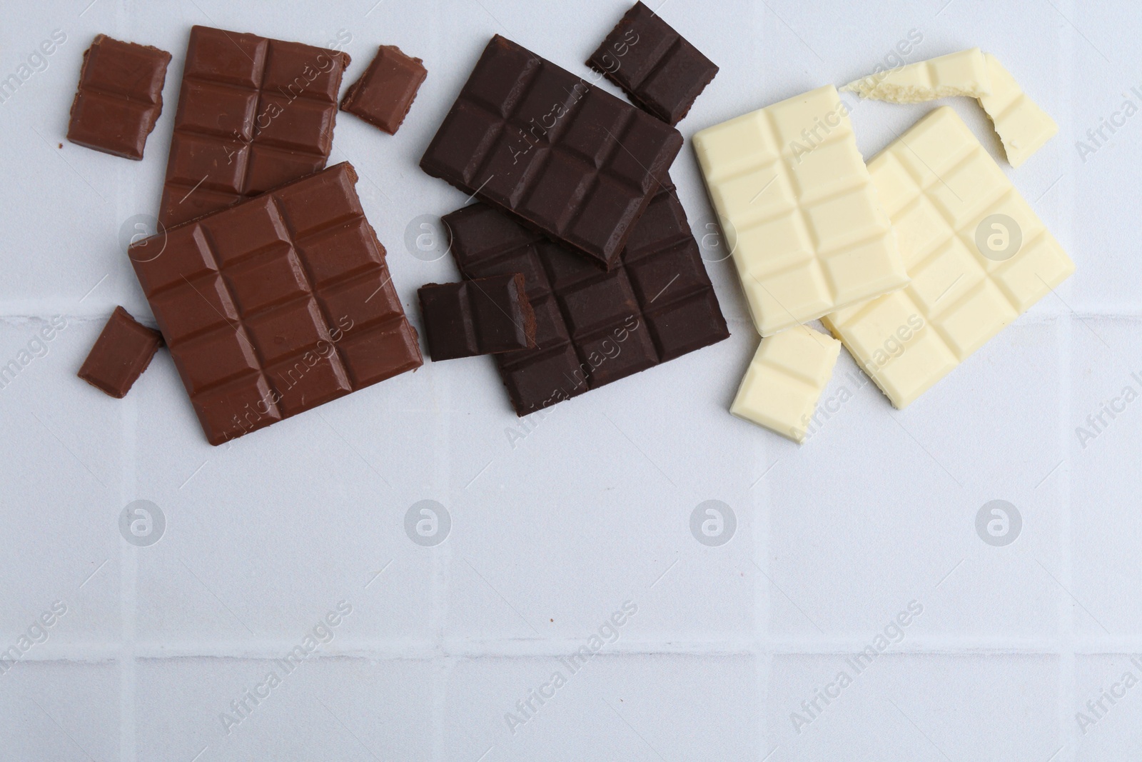 Photo of Different types of chocolate on white tiled table, flat lay. Space for text