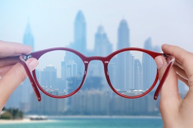 Image of Woman holding glasses against cityscape. View through lenses more clear. Vision correction