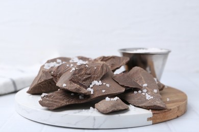 Photo of Pieces of tasty chocolate with salt on white tiled table, closeup