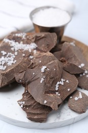 Photo of Pieces of tasty chocolate with salt on white table, closeup