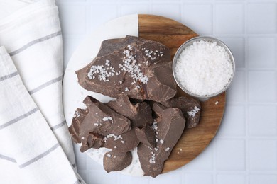 Photo of Pieces of tasty chocolate with salt on white tiled table, flat lay