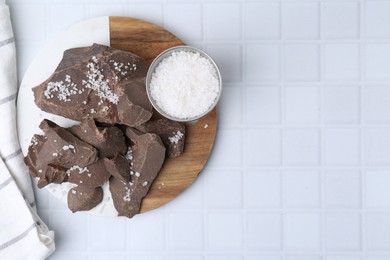 Photo of Pieces of tasty chocolate with salt on white tiled table, flat lay. Space for text