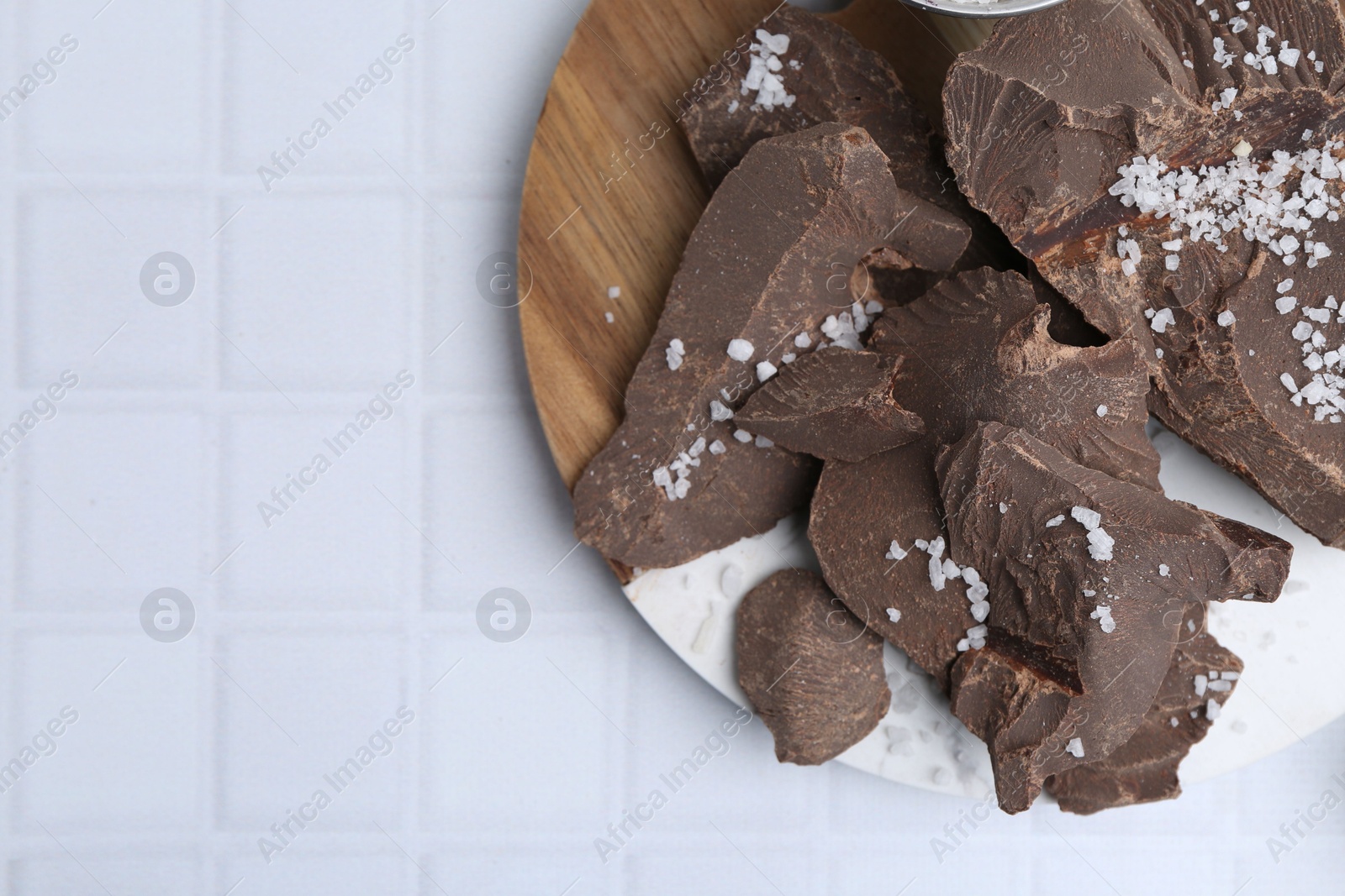 Photo of Pieces of tasty chocolate with salt on white tiled table, flat lay. Space for text