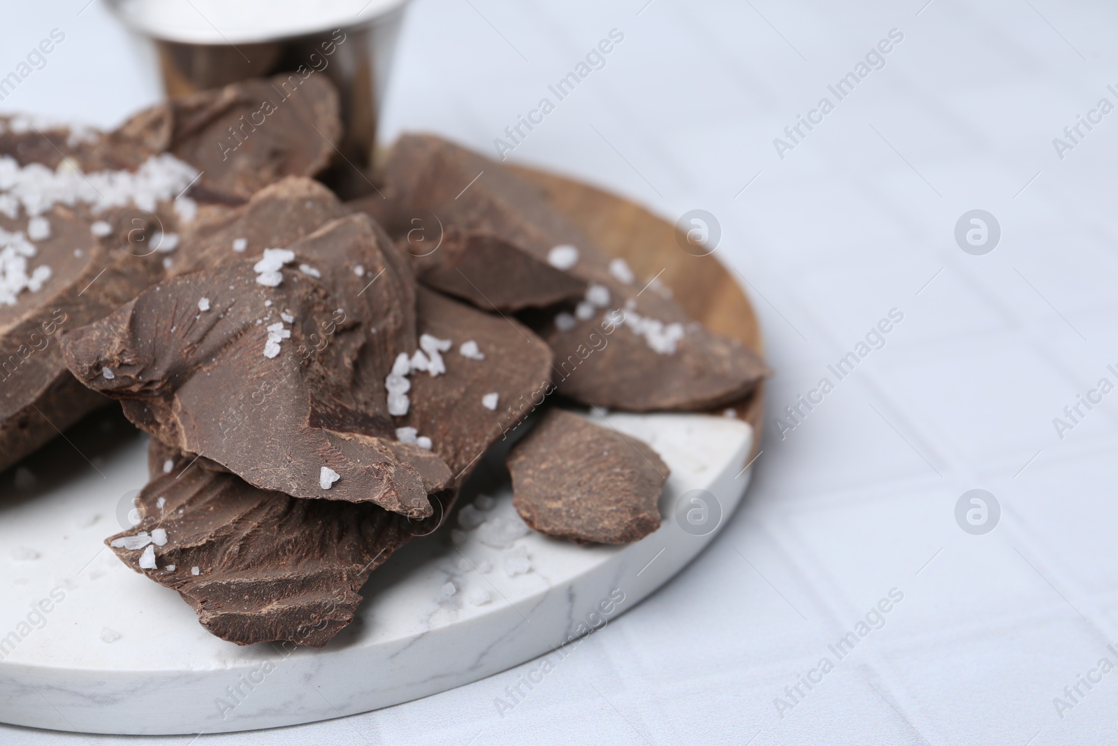 Photo of Pieces of tasty chocolate with salt on white tiled table, closeup. Space for text