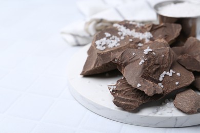 Photo of Pieces of tasty chocolate with salt on white tiled table, closeup. Space for text