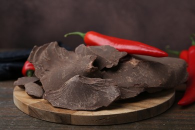 Photo of Pieces of tasty chocolate with chili peppers on wooden table, closeup