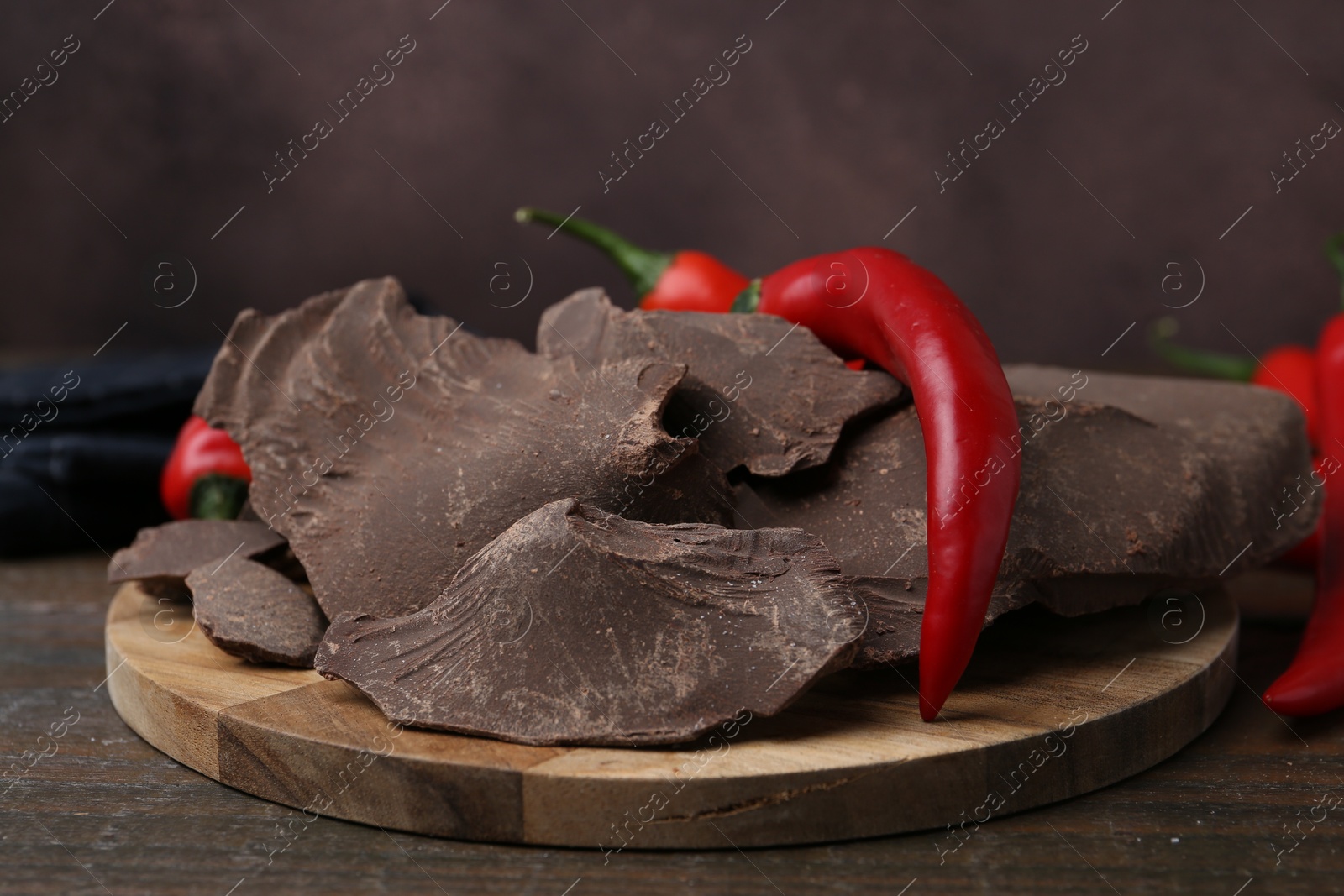 Photo of Pieces of tasty chocolate with chili peppers on wooden table, closeup