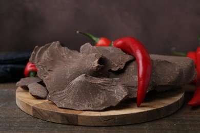 Photo of Pieces of tasty chocolate with chili peppers on wooden table, closeup