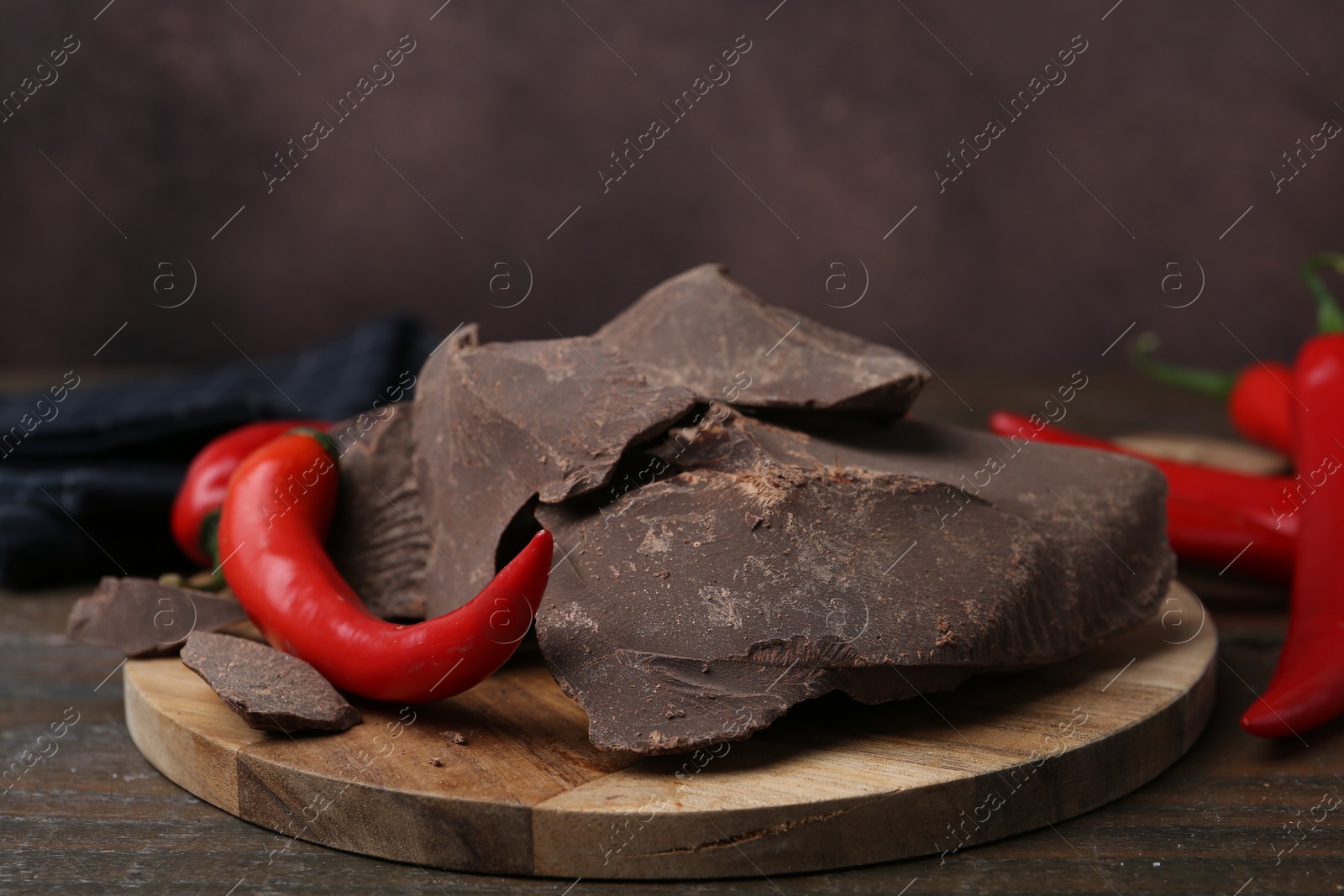 Photo of Pieces of tasty chocolate with chili peppers on wooden table, closeup