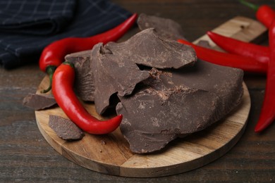 Photo of Pieces of tasty chocolate with chili peppers on wooden table, closeup