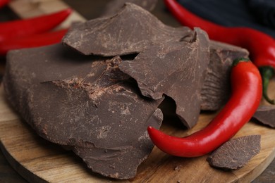 Photo of Pieces of tasty chocolate with chili peppers on table, closeup