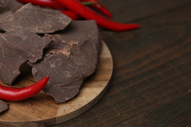 Photo of Pieces of tasty chocolate with chili peppers on wooden table, closeup. Space for text