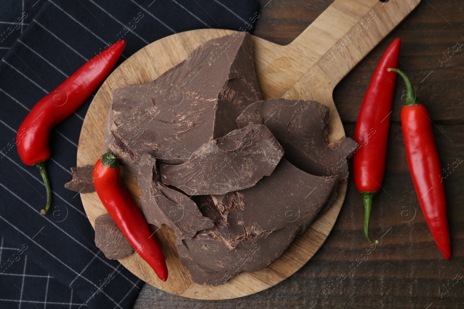 Photo of Pieces of tasty chocolate with chili peppers on wooden table, flat lay