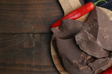 Photo of Pieces of tasty chocolate with chili peppers on wooden table, flat lay. Space for text