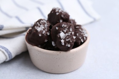 Photo of Tasty chocolate candies with salt in bowl on light table, closeup