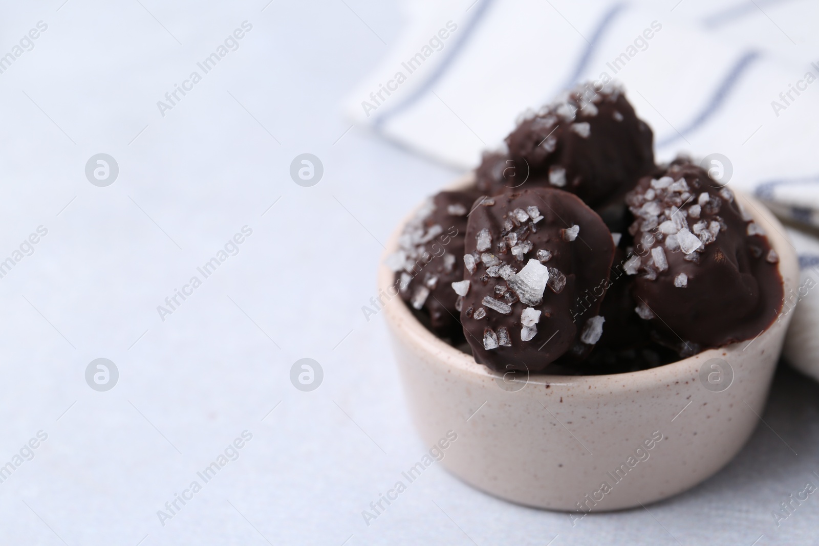 Photo of Tasty chocolate candies with salt in bowl on light table, closeup. Space for text