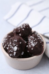 Photo of Tasty chocolate candies with salt in bowl on light table, closeup