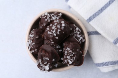 Photo of Tasty chocolate candies with salt in bowl on light table, top view