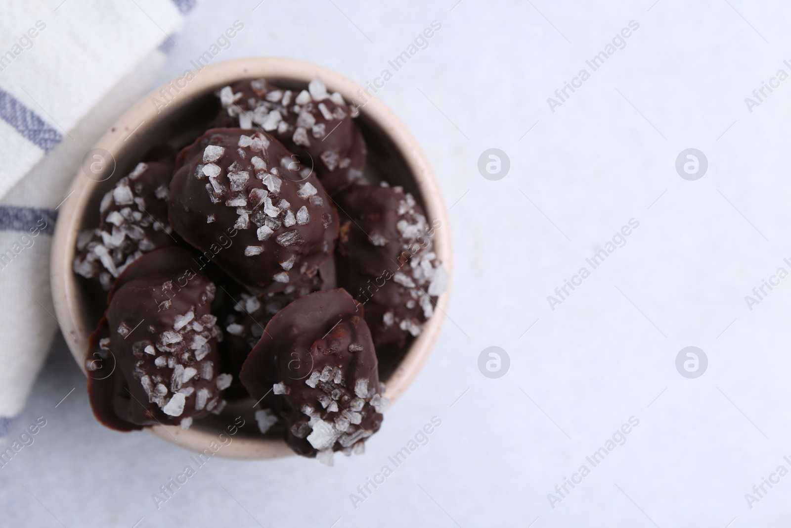 Photo of Tasty chocolate candies with salt in bowl on light table, top view. Space for text