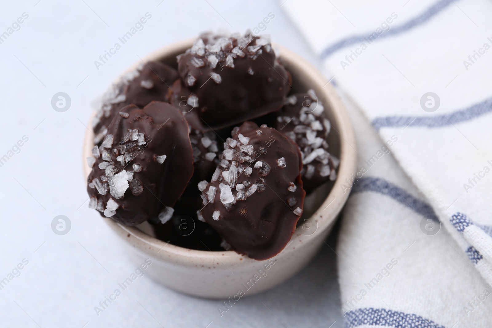 Photo of Tasty chocolate candies with salt in bowl on light table, closeup