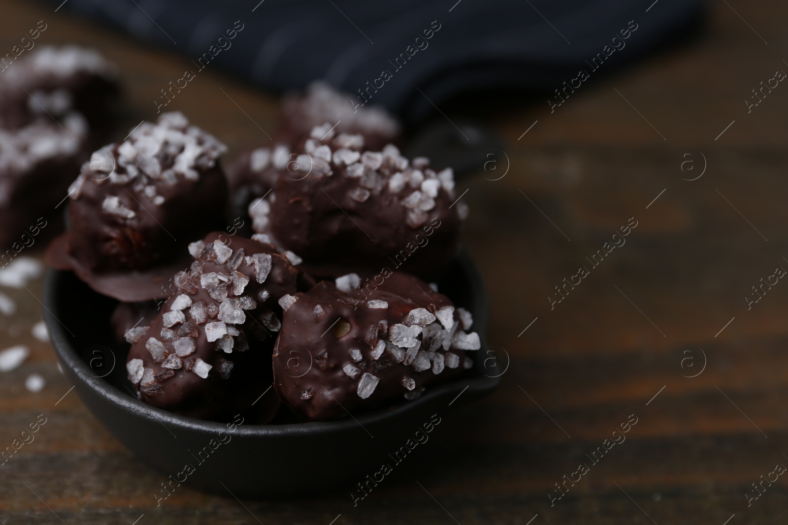 Photo of Tasty chocolate candies with salt in bowl on wooden table, closeup. Space for text