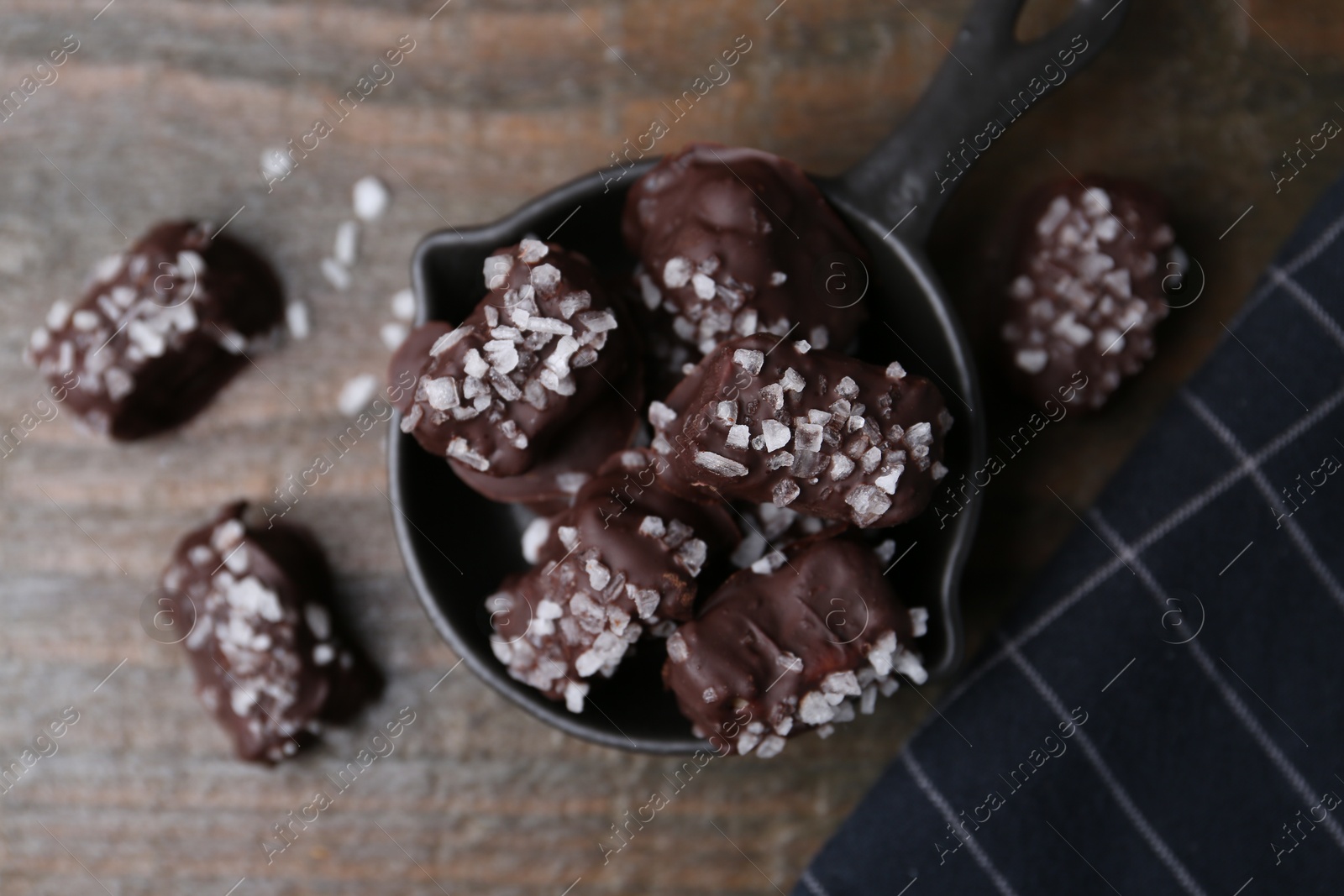 Photo of Tasty chocolate candies with salt on wooden table, flat lay