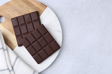 Photo of Pieces of delicious dark chocolate bar on light table, top view. Space for text