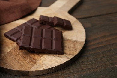 Photo of Pieces of delicious dark chocolate bar on wooden table, closeup. Space for text