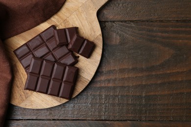 Photo of Pieces of delicious dark chocolate bar on wooden table, top view. Space for text