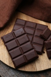 Photo of Pieces of delicious dark chocolate bar on wooden table, closeup