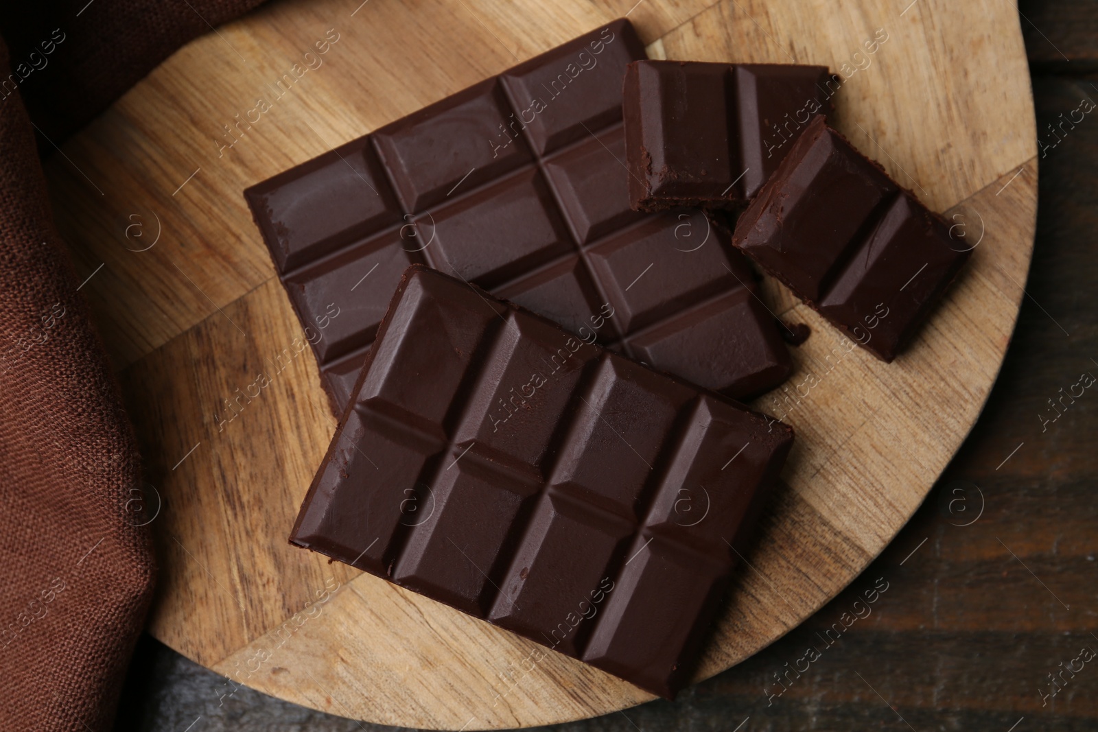 Photo of Pieces of delicious dark chocolate bar on wooden table, flat lay