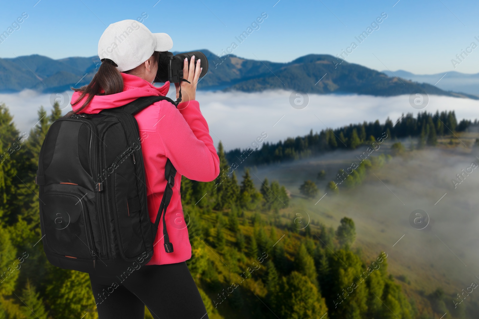 Image of Woman with backpack taking photo in mountains