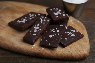 Photo of Pieces of chocolate with salt on wooden table, closeup