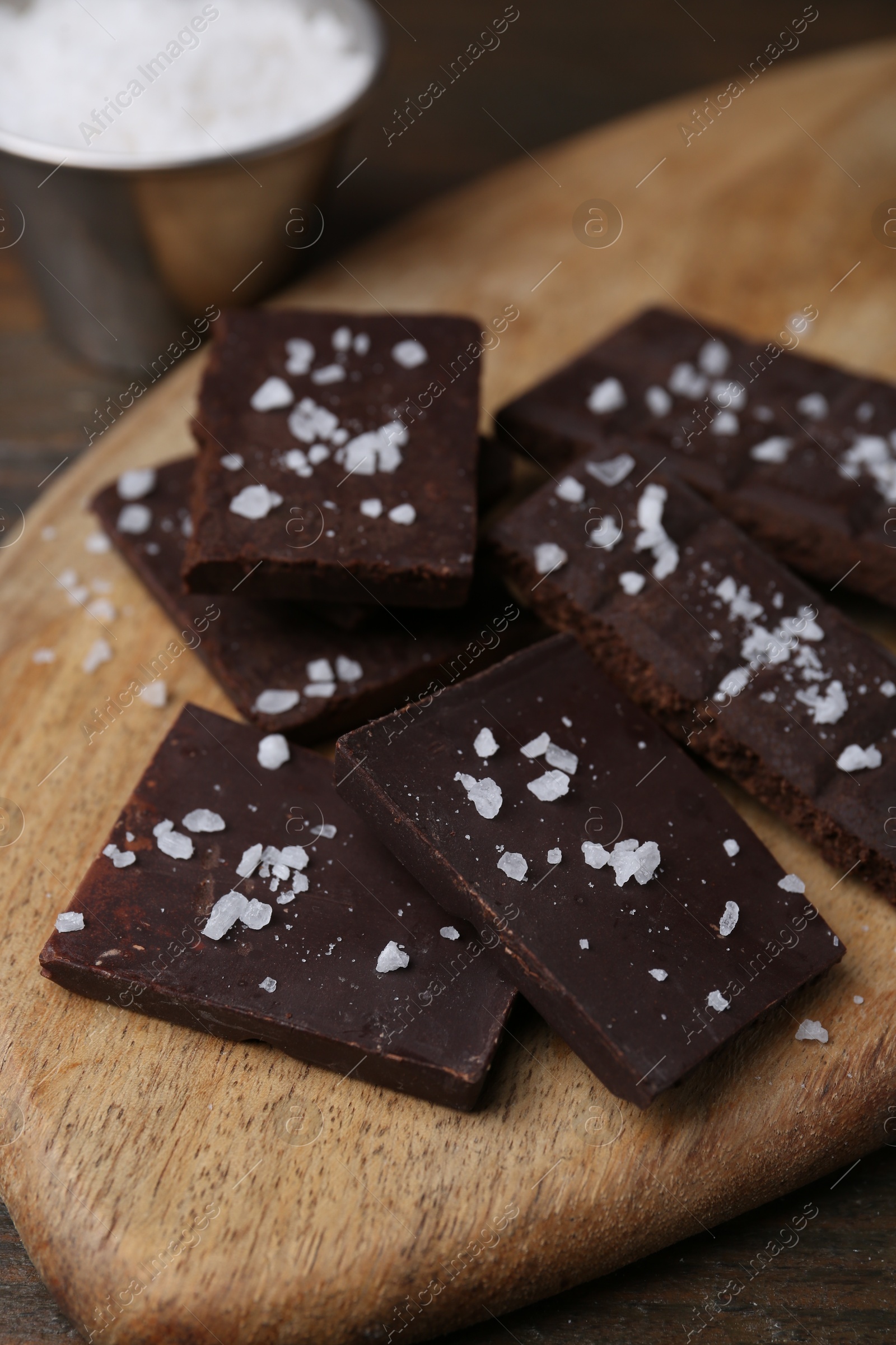 Photo of Pieces of chocolate with salt on wooden table, closeup