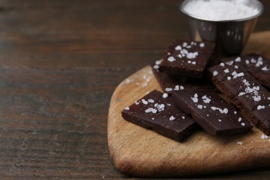 Photo of Pieces of chocolate with salt on wooden table, closeup. Space for text